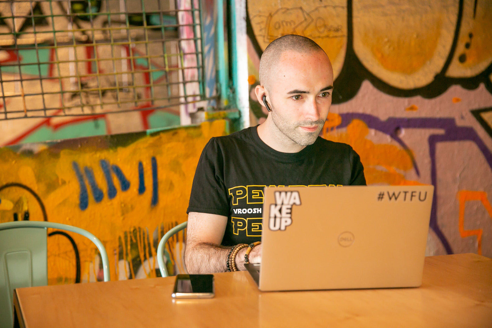 Tom working at a laptop with a graffiti wall behind him, immersed in focus and disconnected from the world around him